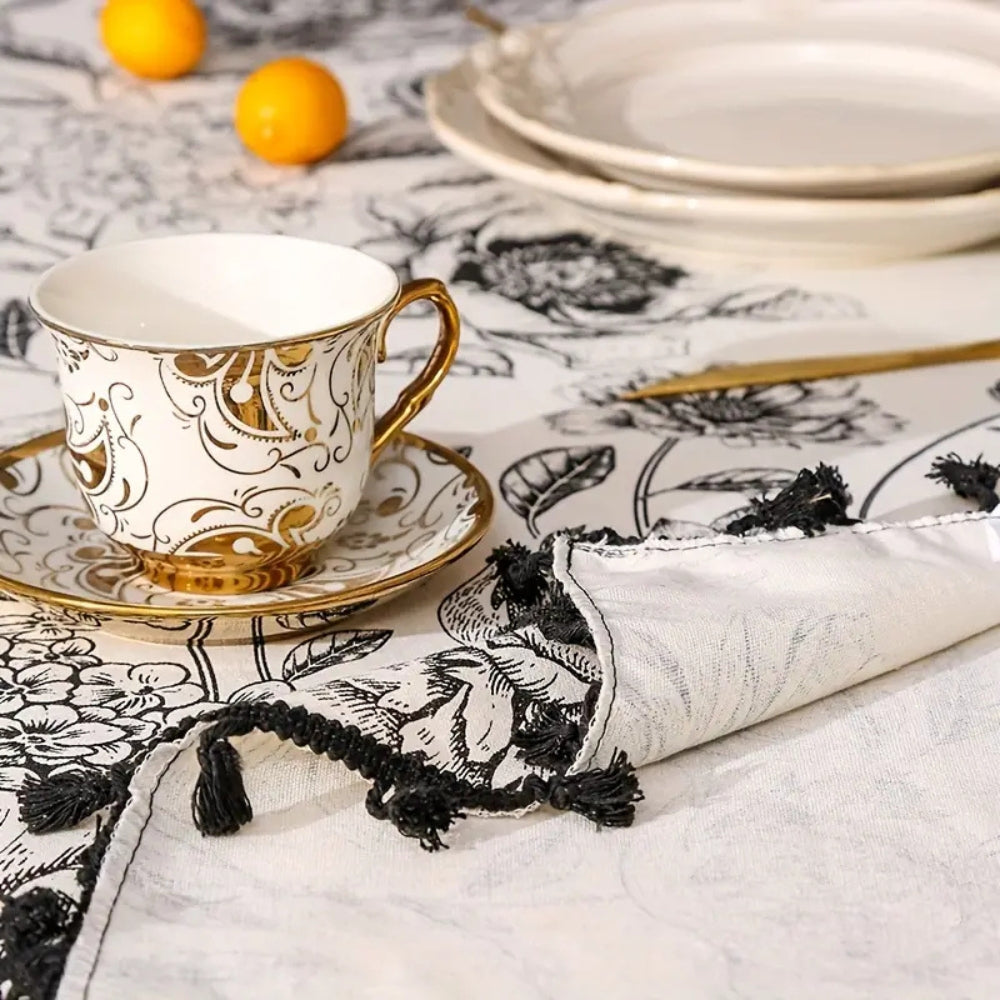 Detail view of black floral tasseled farmhouse tablecloth with intricate floral patterns and a rustic touch.